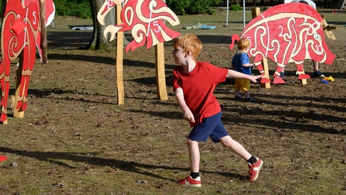 A young boy throwing a bean bag at oversized wooden cut-outs of Anglo-Saxon era animals in the grounds of Sutton Hoo